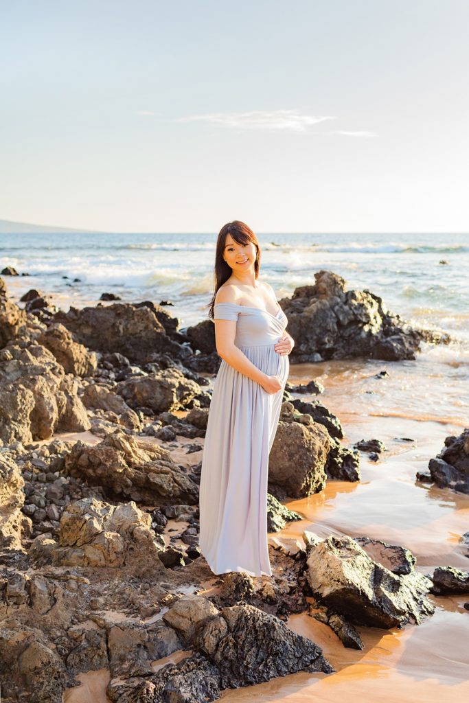beautiful and pregnant asian woman poses on volcanic rocks during her Wailea babymoon portraits at sunset with Love + Water Photography