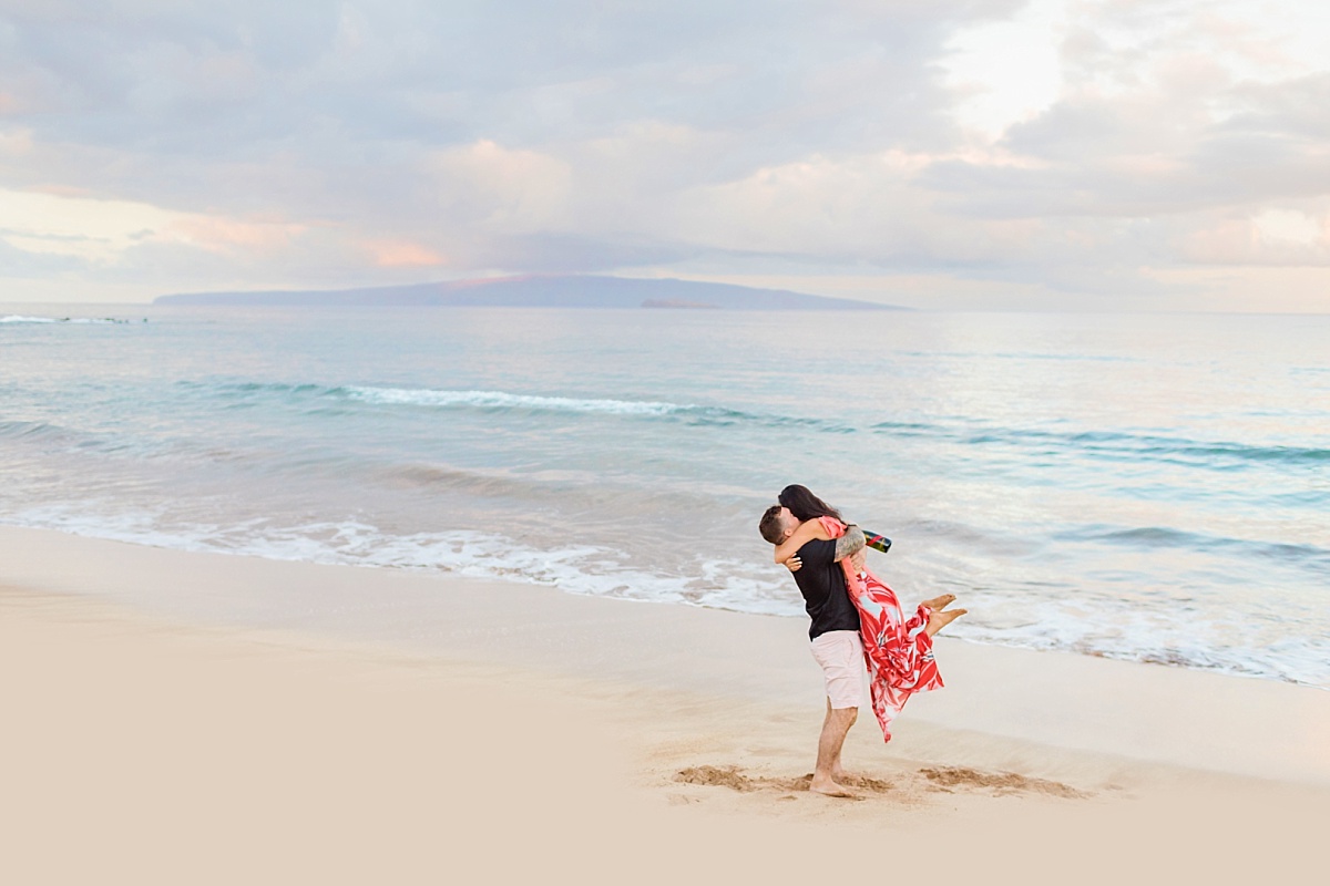 A man embraces and picks up his new fiance at an engagement session in Maui after she says yes to his beach proposal.