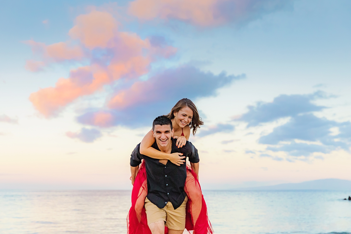 Woman on her fiance's back as they both laugh and smile at the camera during Maui beach photoshoot