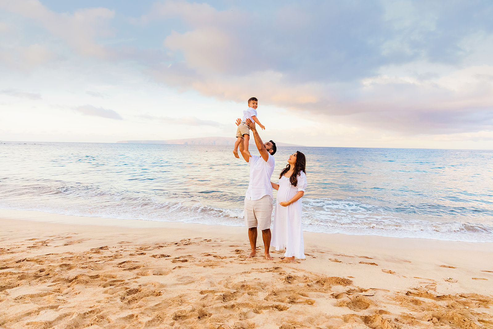 Father looks up at his son and smiles at the camera during a beach photoshoot in Kihei
