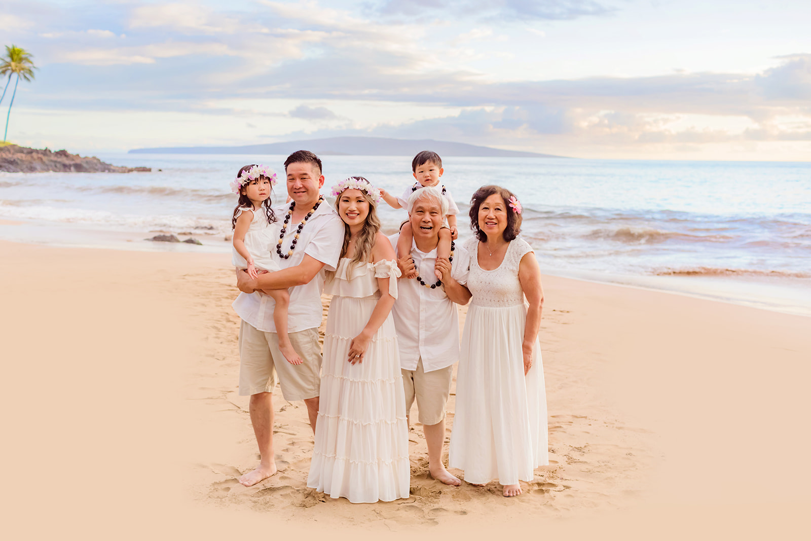 Family of six dressed in cream colors smile at the camera for sunrise during their Maui photoshoot