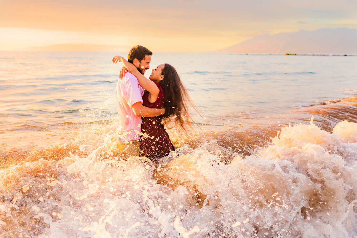 A couple smiles and embraces in the ocean while taking beach photography on Maui at sunset with Love + Water Photography.