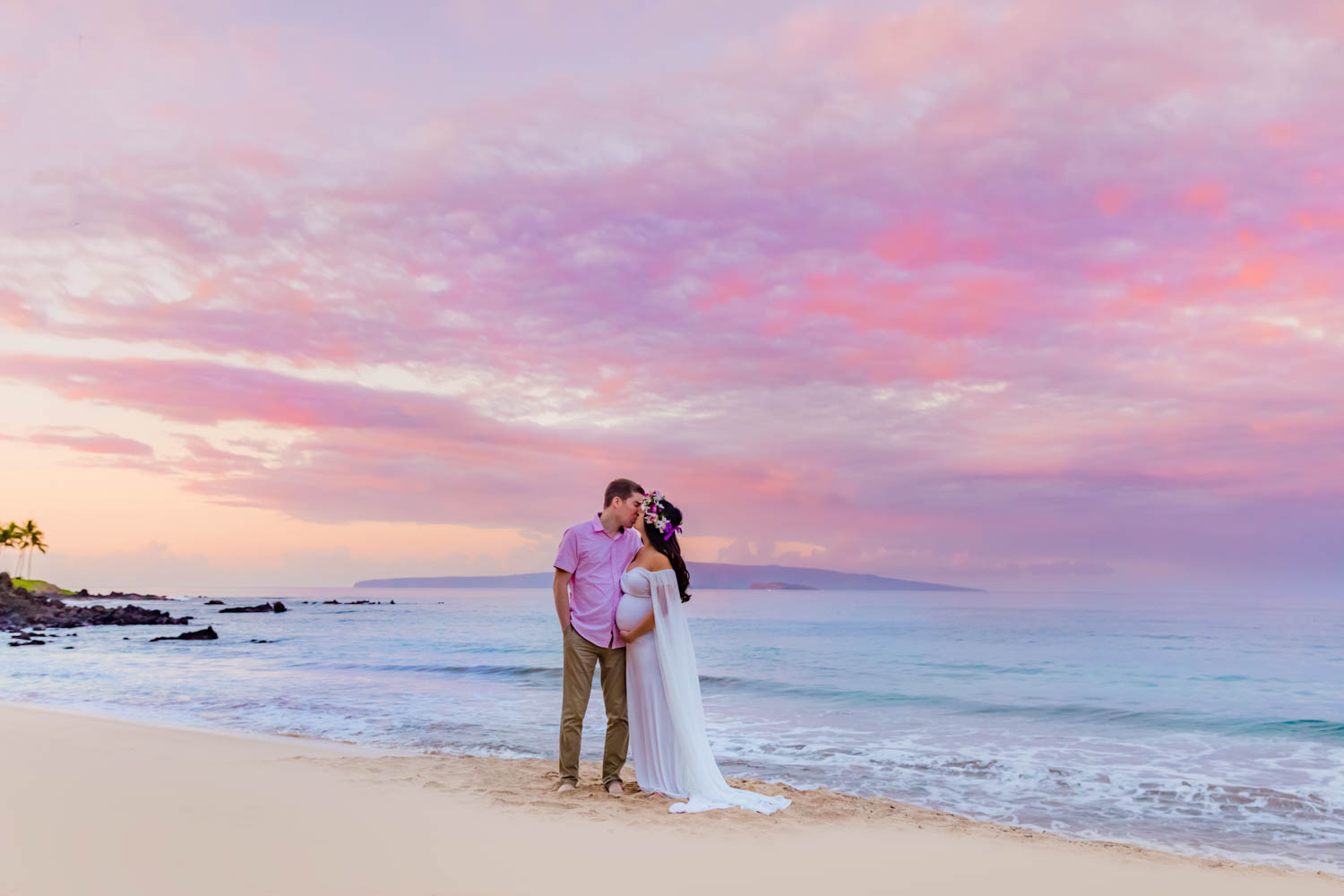 A couple kisses during a babymoon photoshoot on the beach in Maui during sunset with Love + Water Photography.