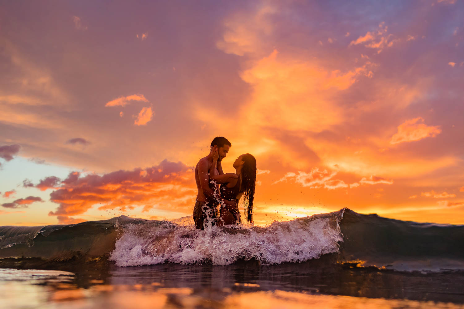 A couple looks into each other's eyes while standing in the ocean during a fiery sunset for beach photography on Maui. 