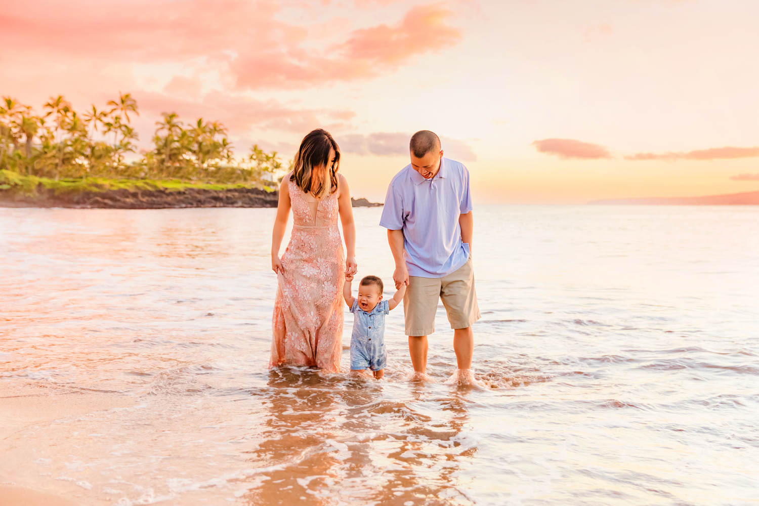Two parents walk in the water while holding their child's hands while taking family beach photos on Maui. 