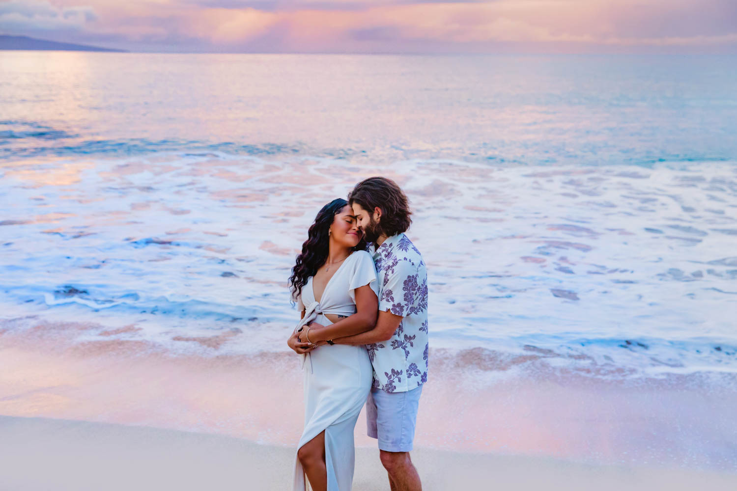 A couple embraces lovingly in front of the ocean during a sunrise beach photography session on Maui, Hawaii.