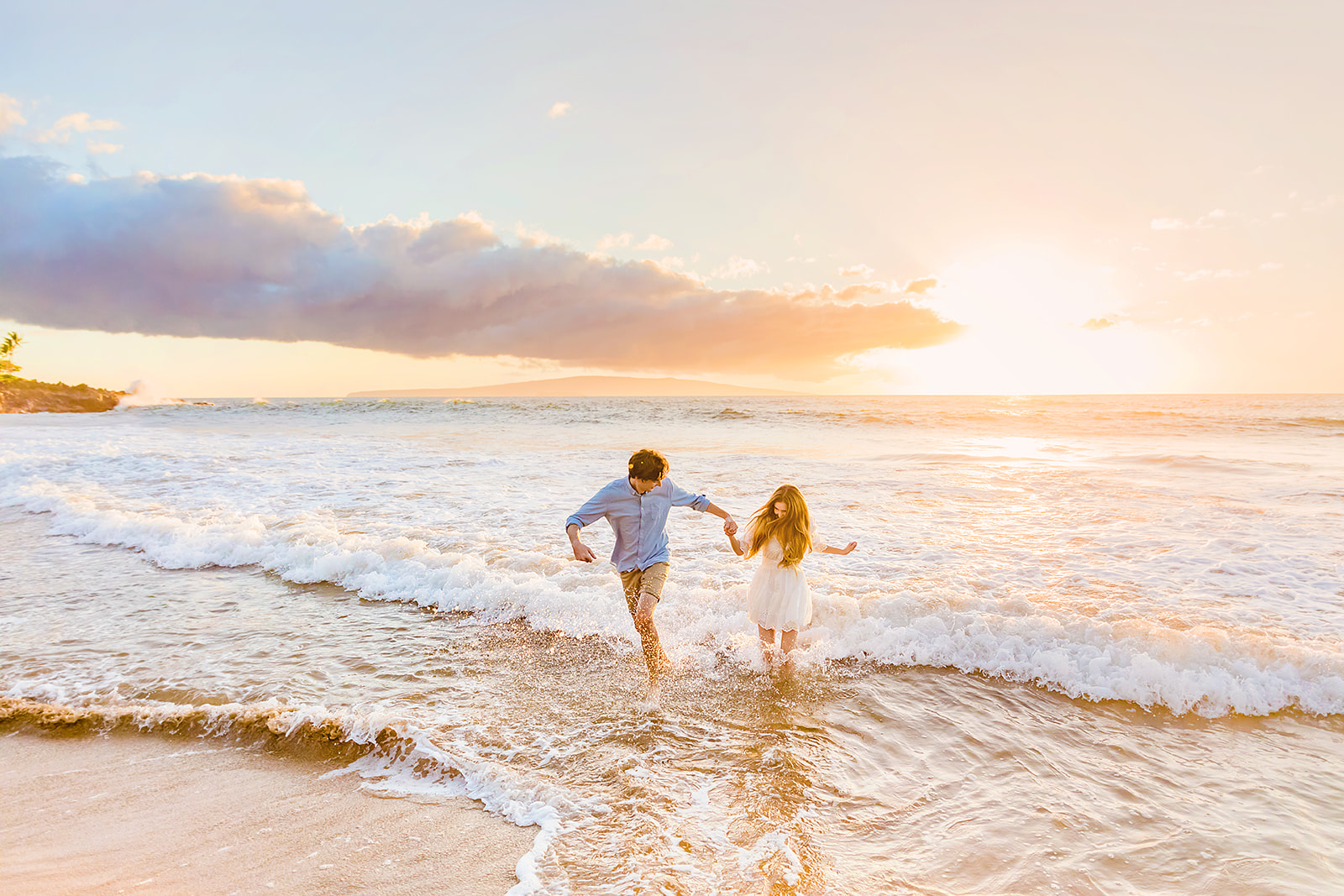 Mia Maples and her fiance run through the water while posing for sunset engagement photos on the beach in Wailea, Maui. 