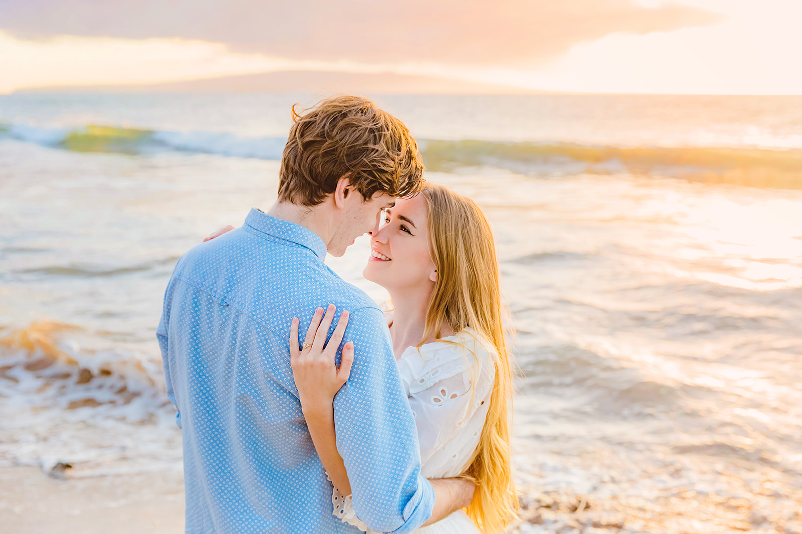 A couple embraces and stares each other in the eyes on the beach for Mia Maples Maui engagement photos with Love + Water Photography. 