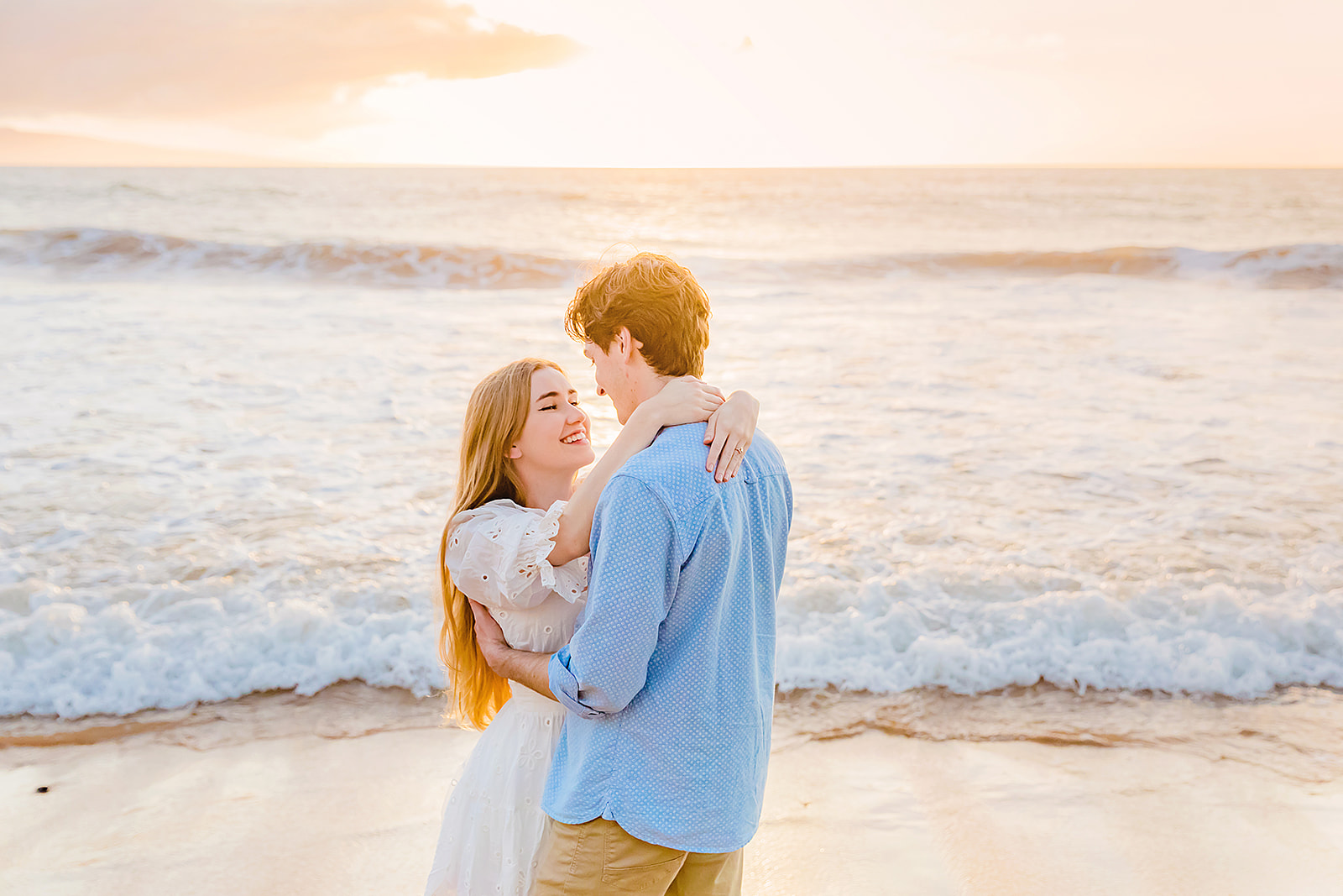 Love + Water Photography captures Mia Maples Maui engagement photos on the beach as she embraces and smiles at her fiance in front of the ocean.