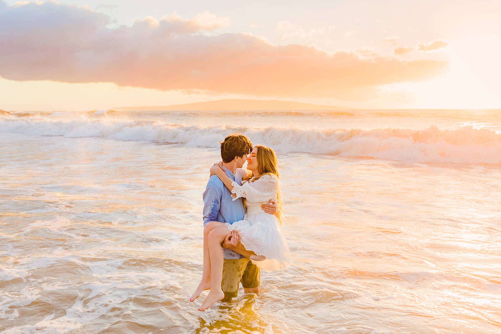 Mia Maples is carried by her fiance into the ocean during sunset beach engagement photos with Love + Water Photography in Hawaii.