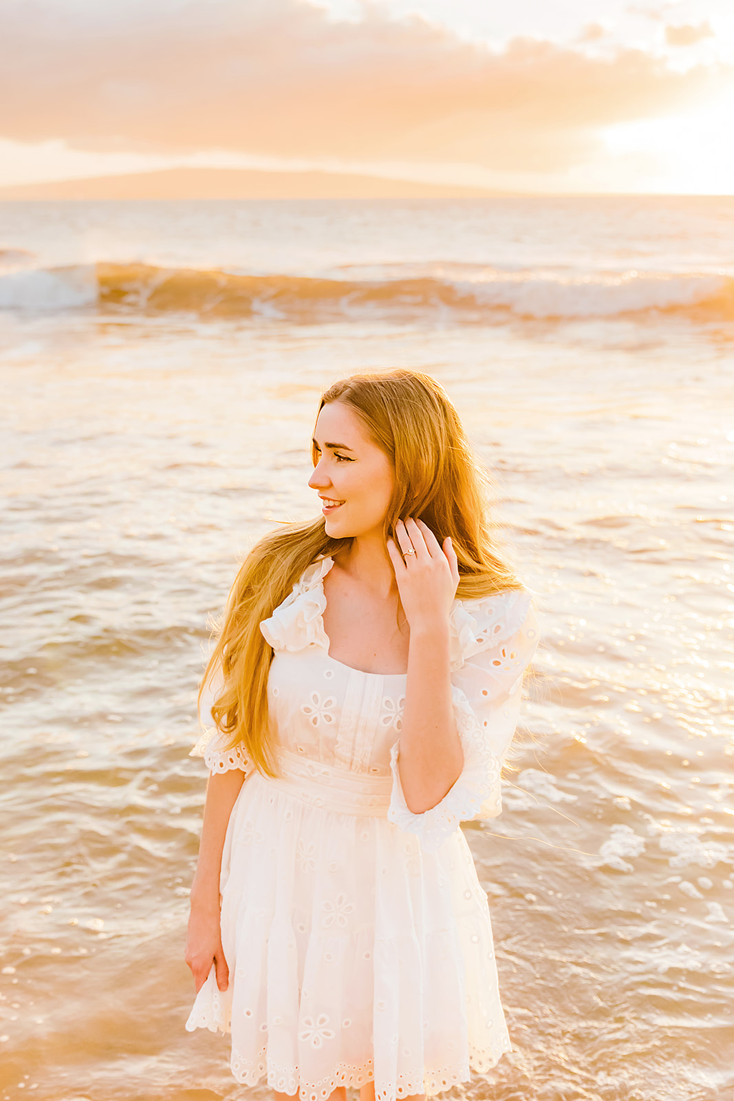 YouTube influencer Mia Maples wearing her engagement ring and an adorable white dress poses for sunset engagement photos on the beach in Maui.