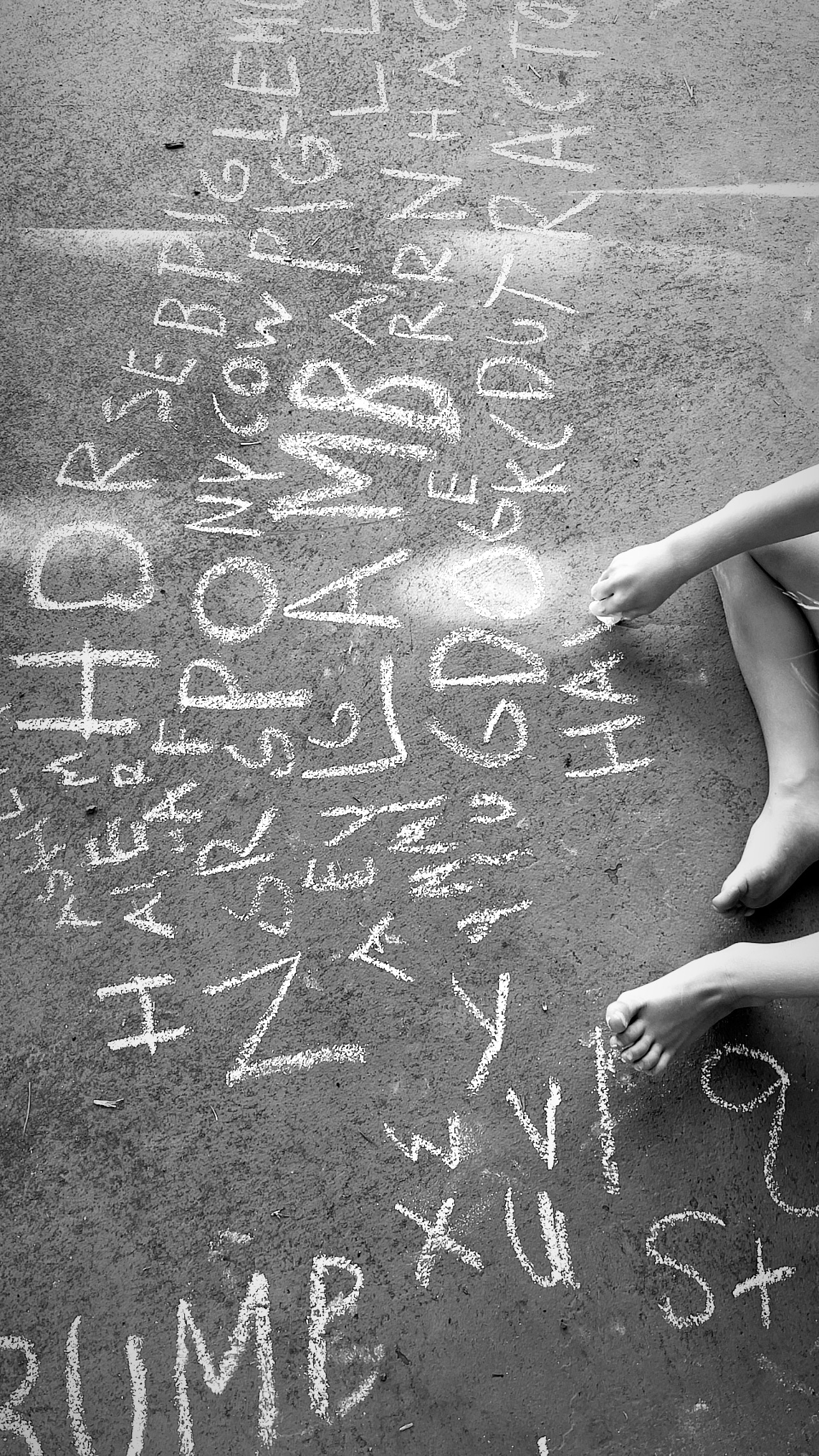 Black and white image of toddler writing the alphabet on the concrete during lockdown in Hawaii in 2020.