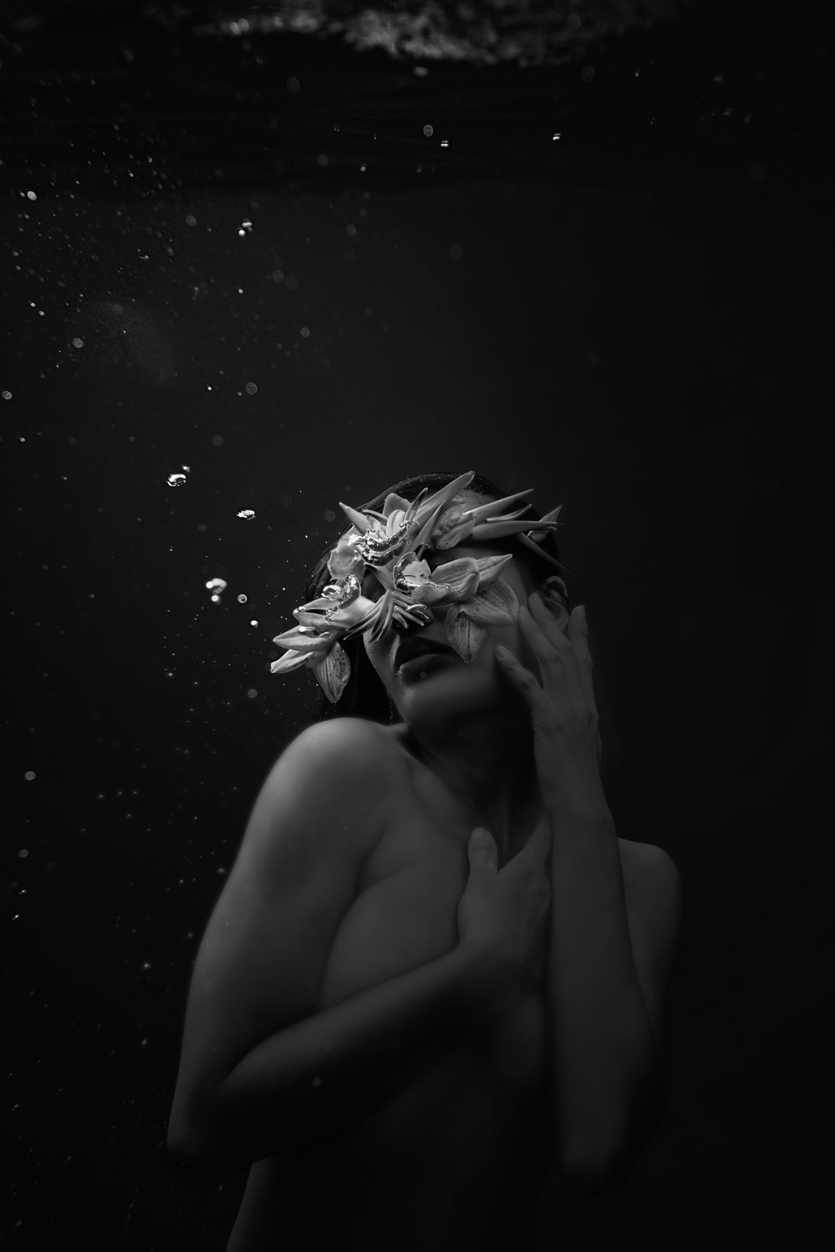 Black and white underwater image of topless woman wearing eye mask made of flowers on Maui