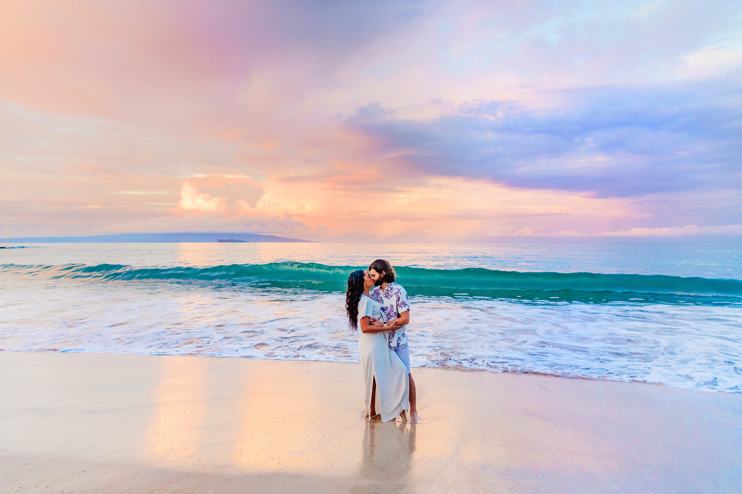 Newly engaged couple kisses on the beach at sunrise after being photographed by Love and Water Photography on Maui.