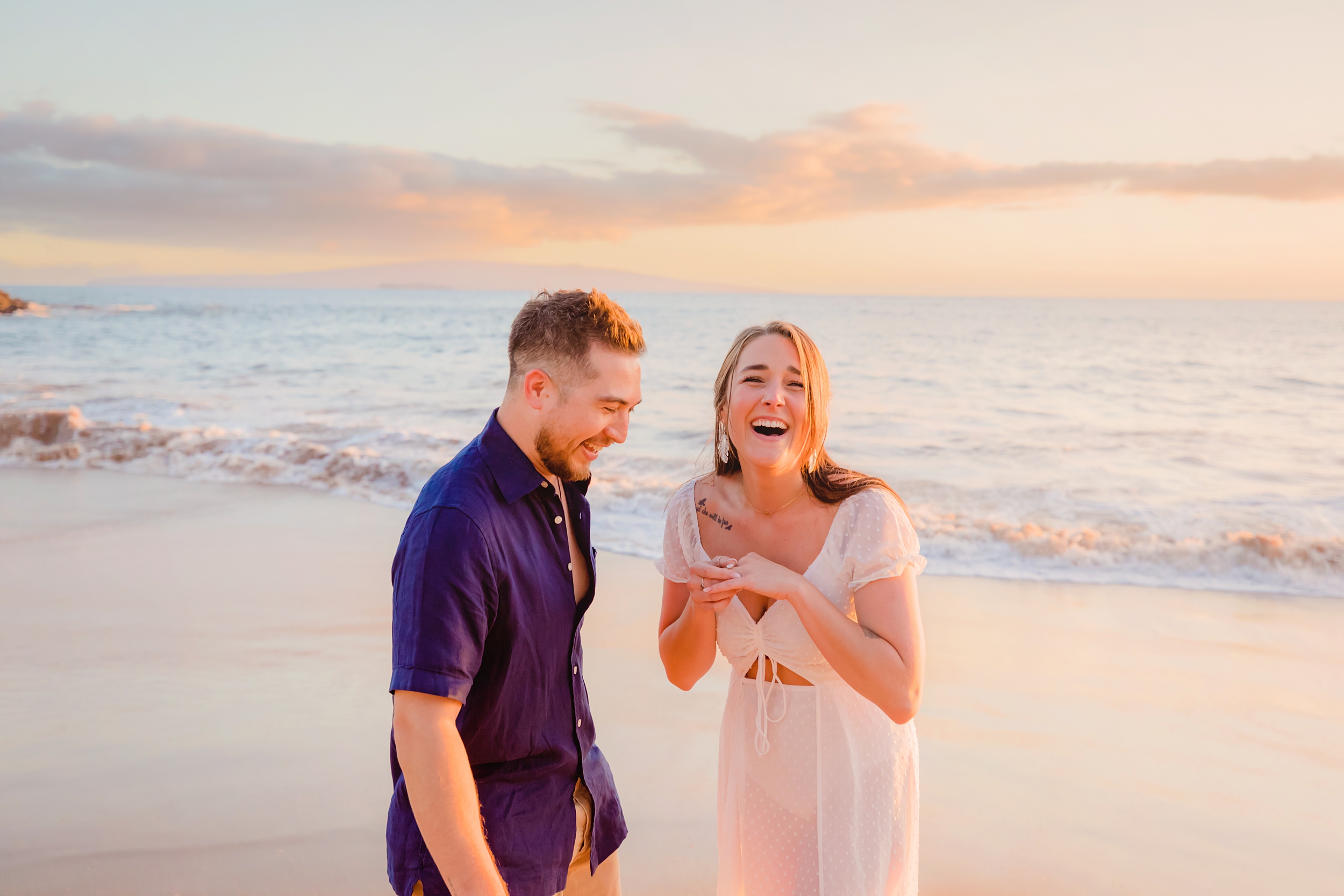 Woman looks at the camera and laughs while holding her engagement ring after her boyfriend proposes to her on the beach in Wailea.
