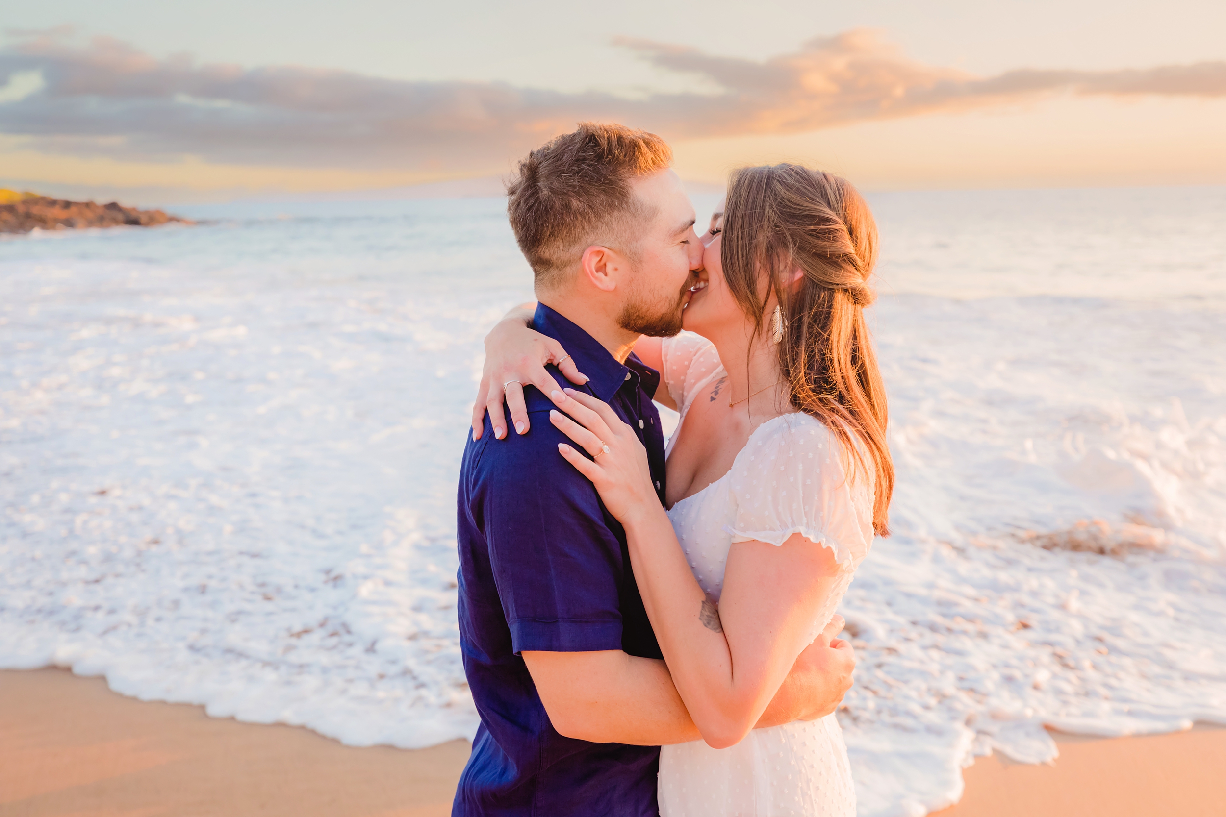 Happy young couple with brown hair smile and kiss one another after a surprise Maui proposal in Hawaii.