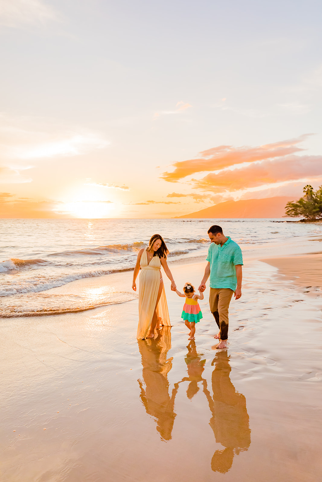 A mother and father walk while holding hands with their young daugher during sunset beach family photos in Hawaii with Love + Water Photography.