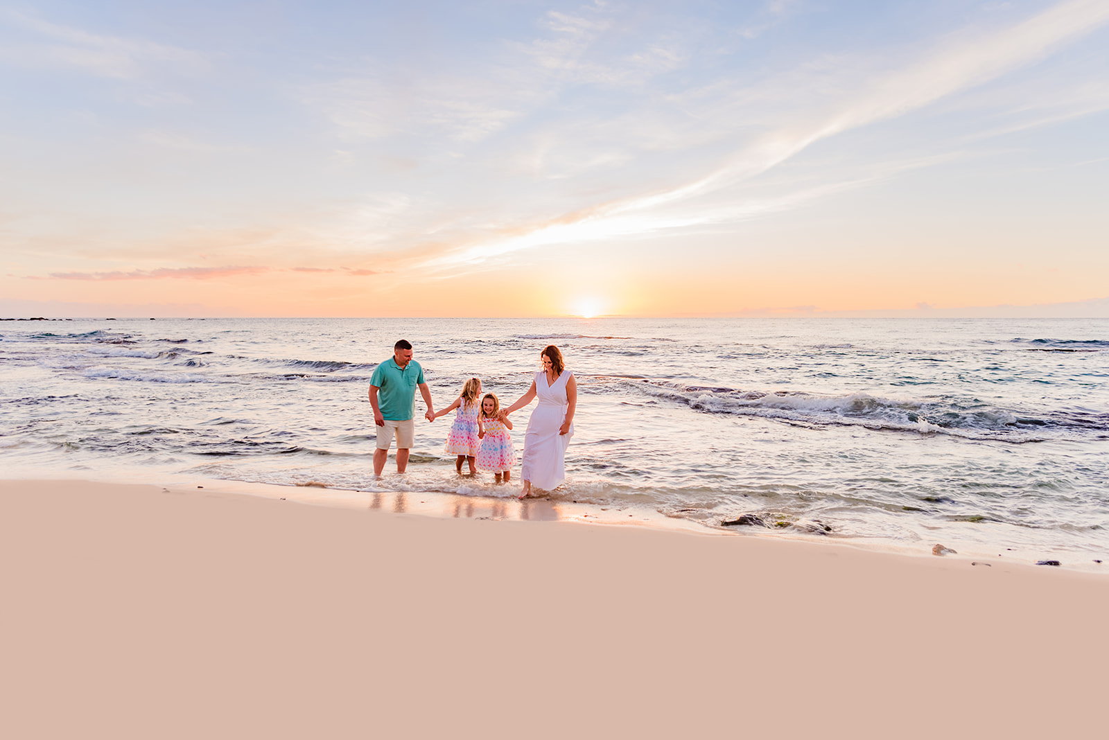 A mother, father, and two young daughters walk together in the waves during a beach family photo session on Maui, one of the best family photo locations in Hawaii.