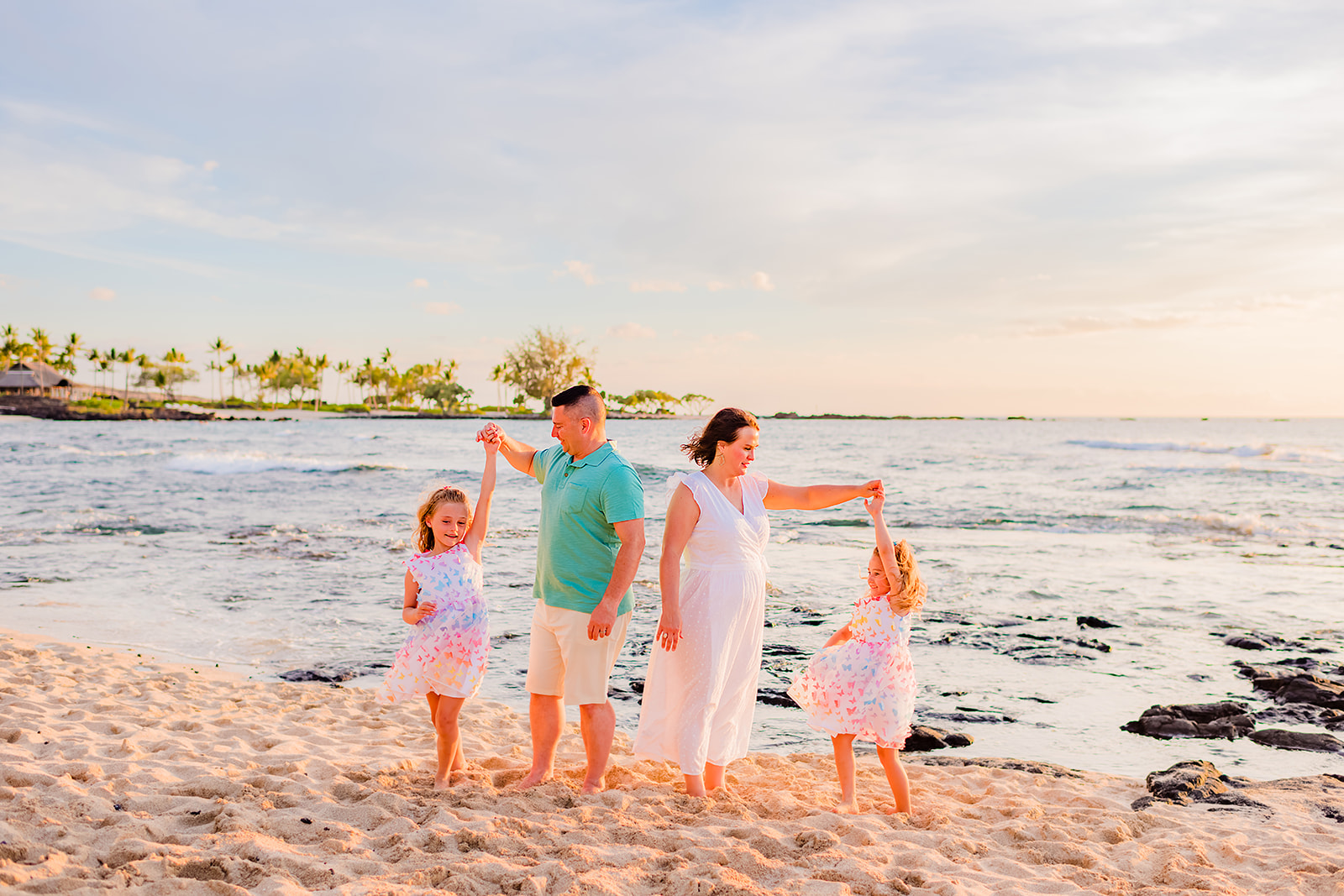 A mother and father play with their two young daughters while taking professional family beach photos on Hawaii.