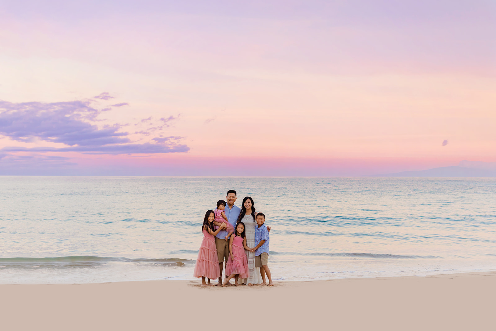 A young family of six stands together for beach family portraits at sunrise on Hawaii.