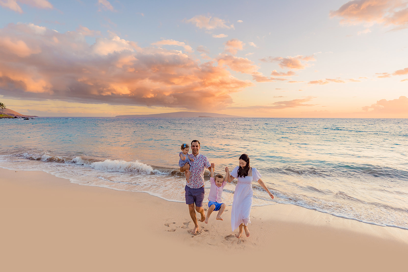 A family with two parents and two children walk playfully together on during family beach pictures on Maui.