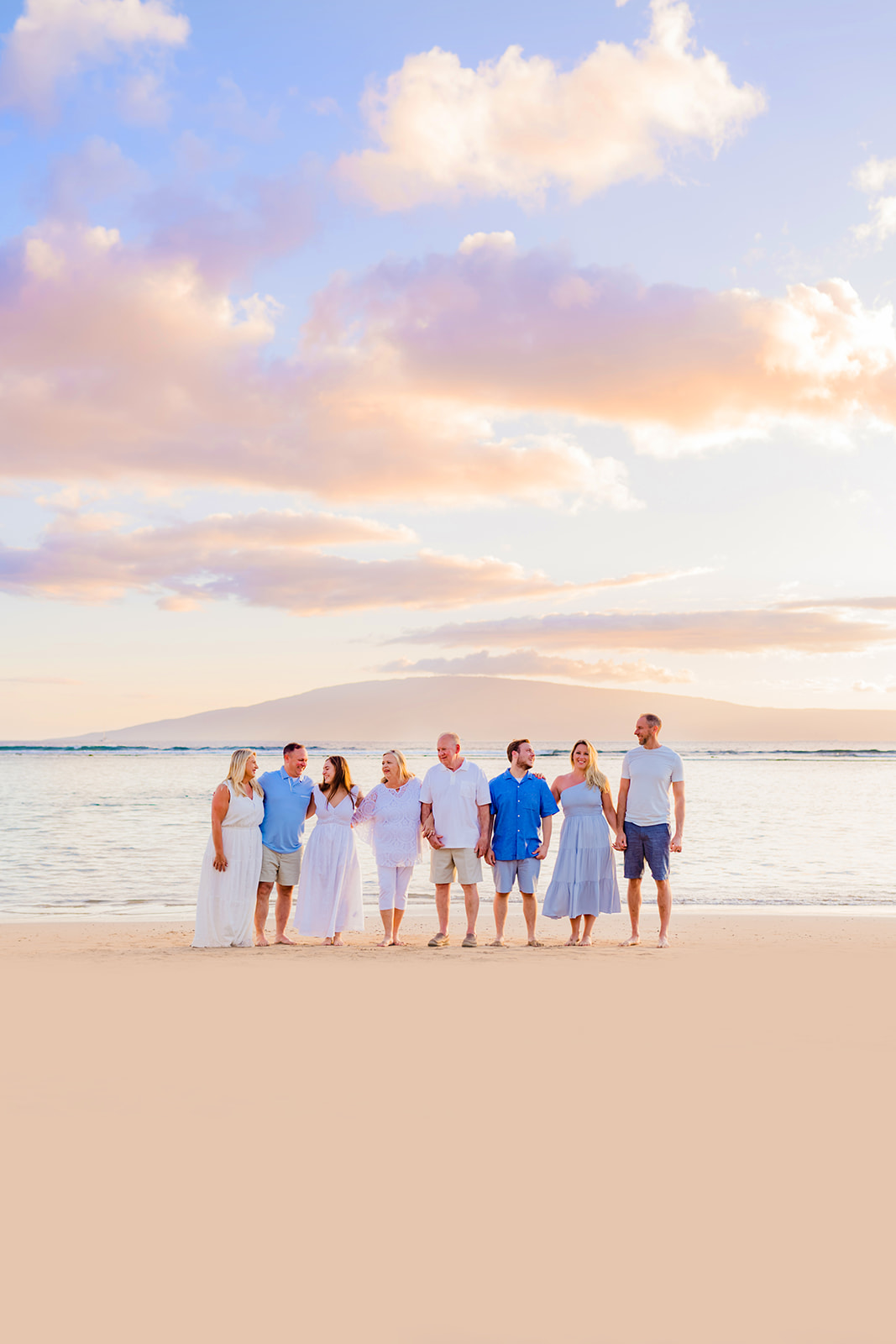 A large family wearing white and blue stand together on the beach during family photos at Sunset on Maui.