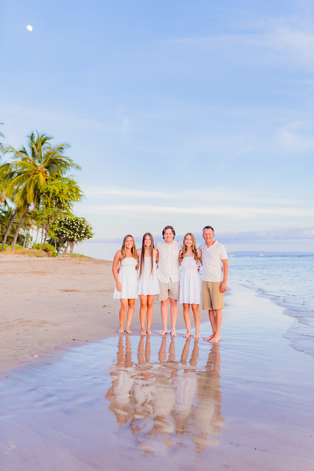 A group of teenage siblings stand together wearing all white and cream for family beach pictures on Hawaii with Love + Water Photography.