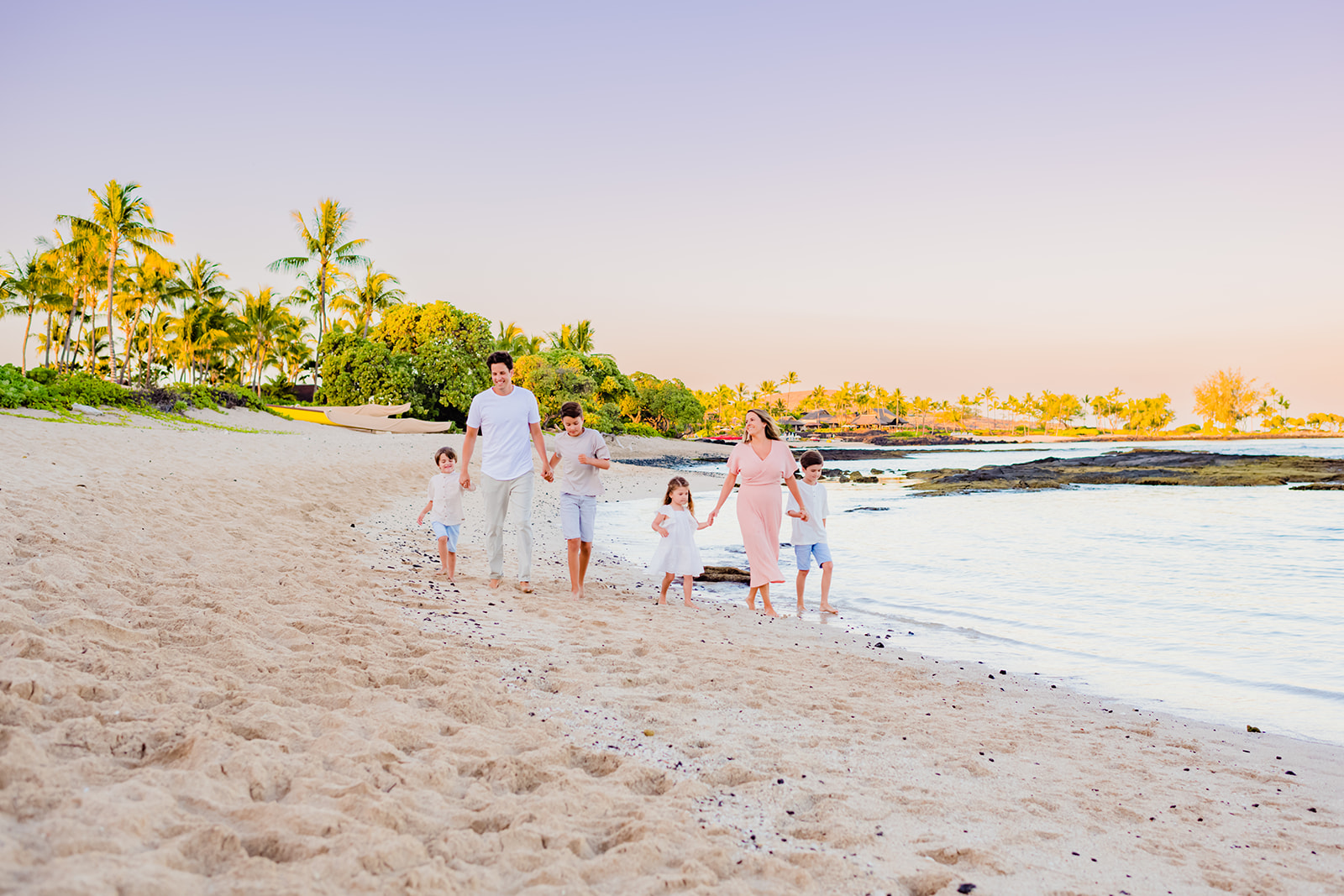 A family with two parents and four children walk hand-in-hand on the beach while taking professional family pictures in Hawaii.