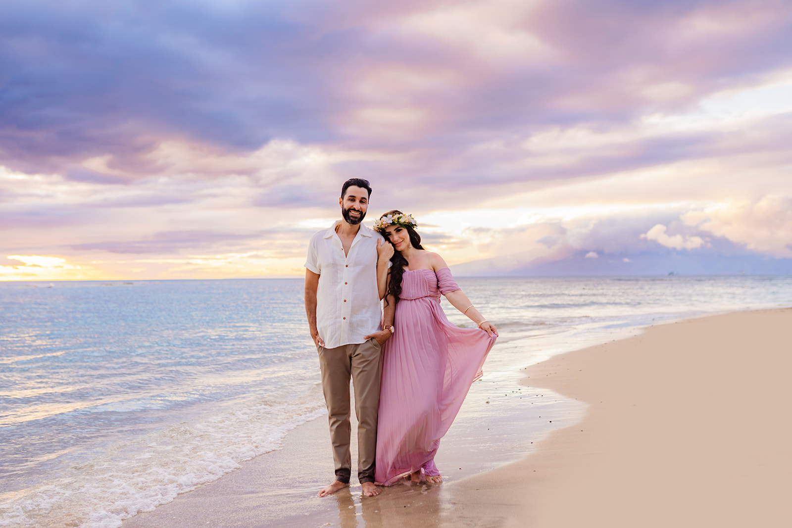 woman in pink dress holds hands with her partner and leans into his shoulder during their sunset maternity photoshoot in west maui