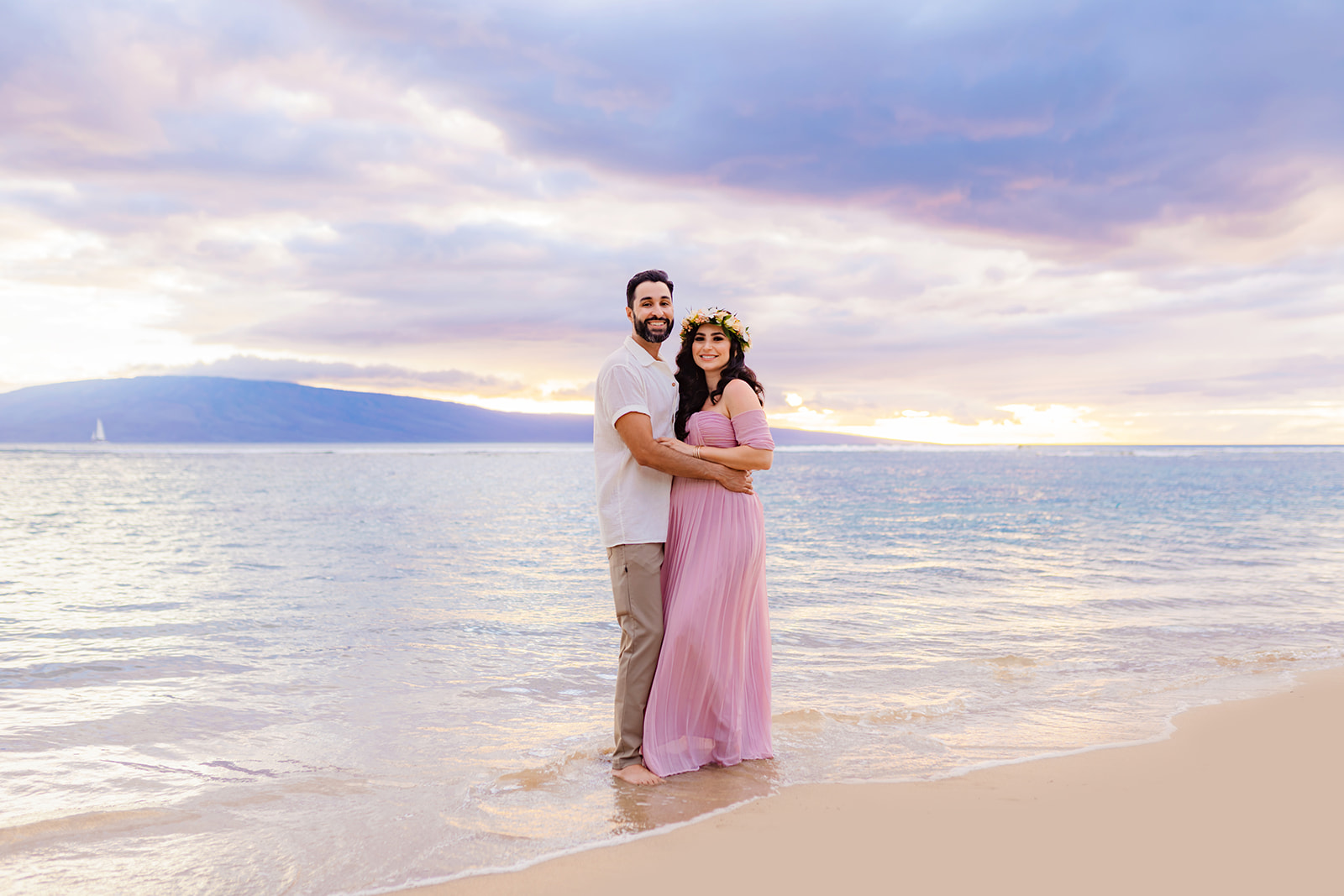man and his pregnant wife smile at the camera of their maternity photographer during their babymoon session in Hawaii