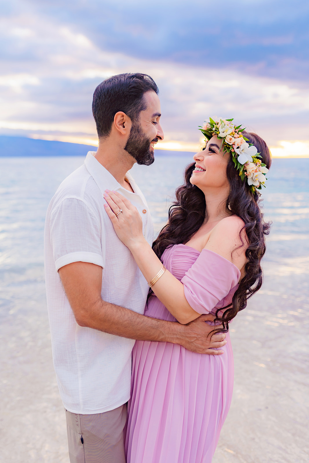 mom-to-be looks lovingly into the eyes of her partner on the beach in Maui during their maternity session