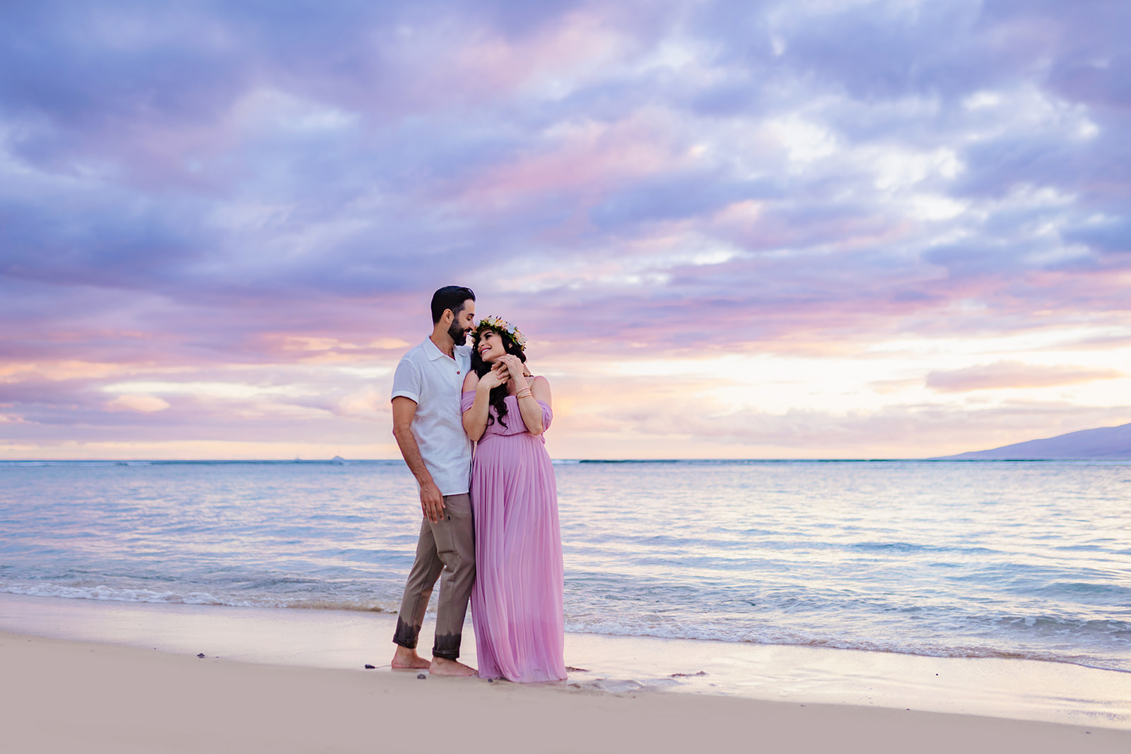 Mother-to-be leans back in the arms of her partner under a pastel sky during their maternity photoshoot in West Maui