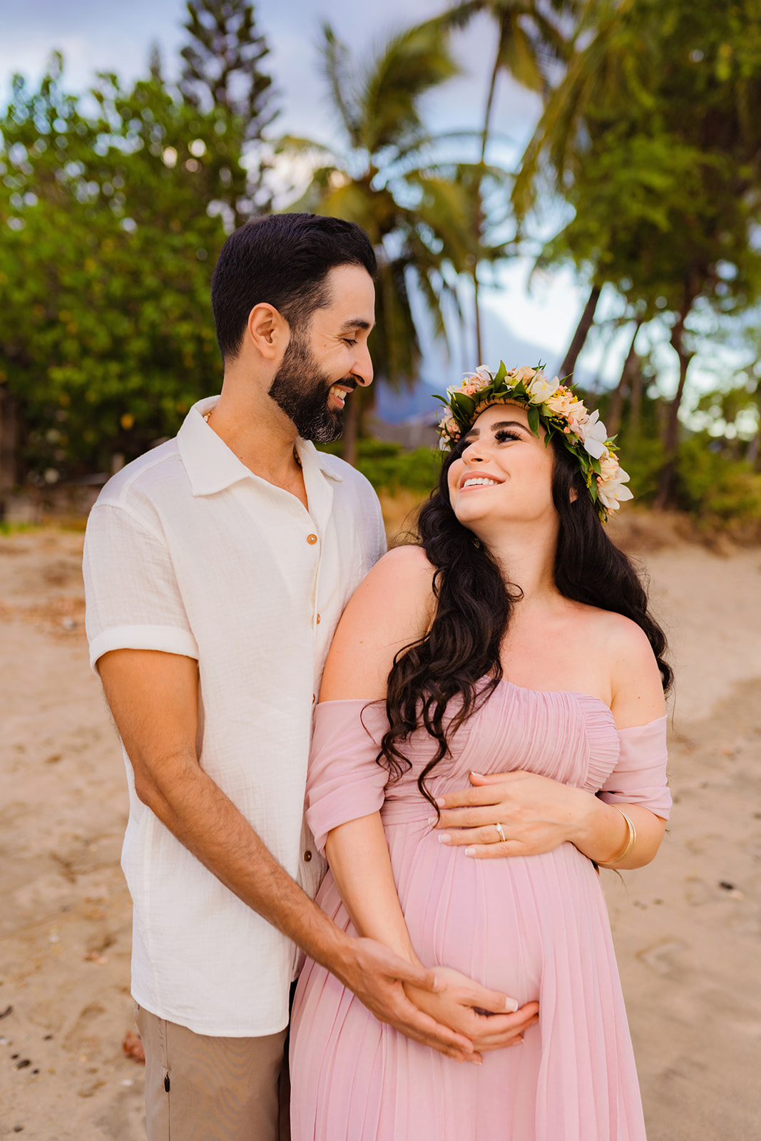 man and woman flash big smiles towards eachother in west maui on the beach during their maternity session
