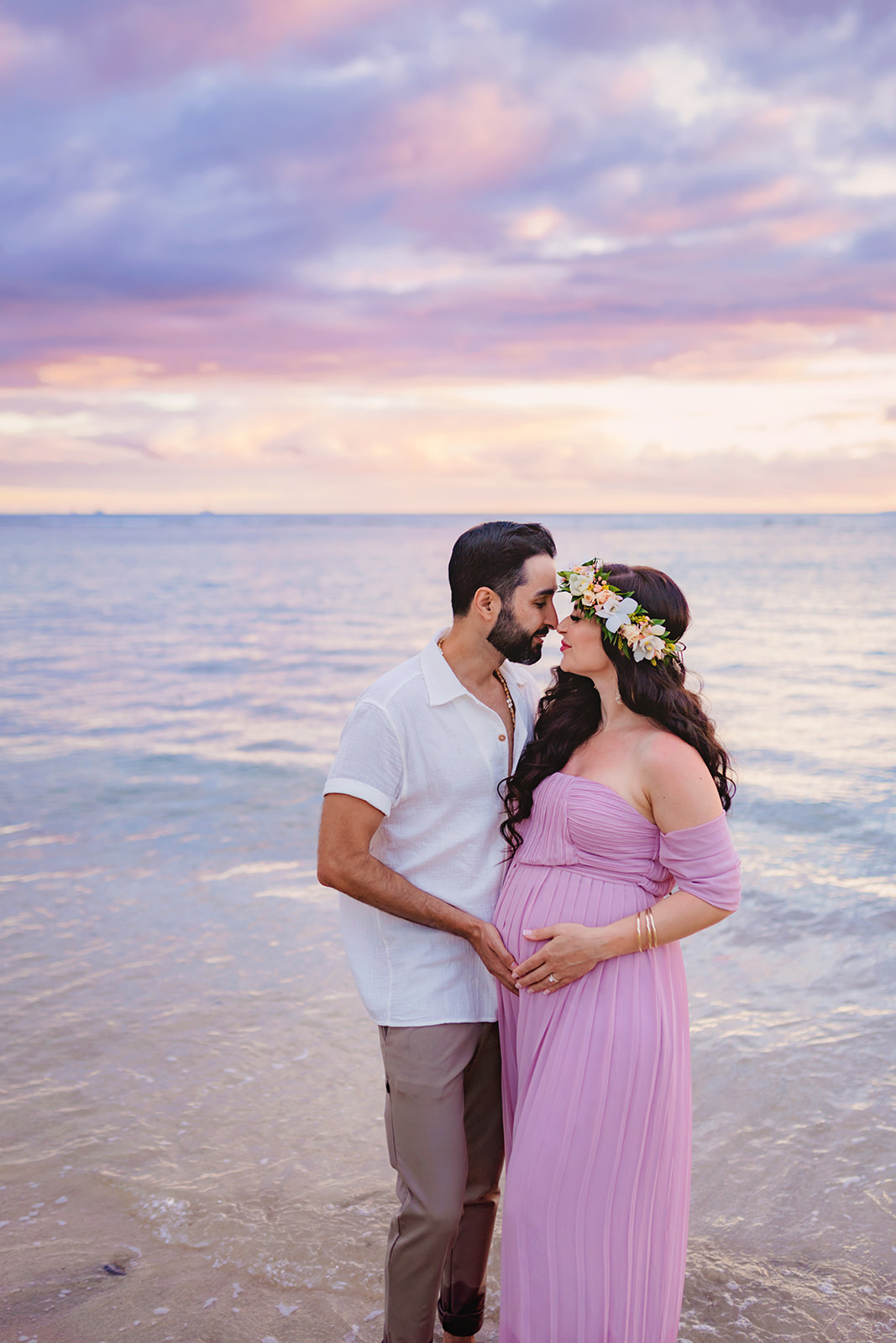 man and woman stand nose to nose with their eyes closed as they stand in ankle-high water during their maternity photoshoot