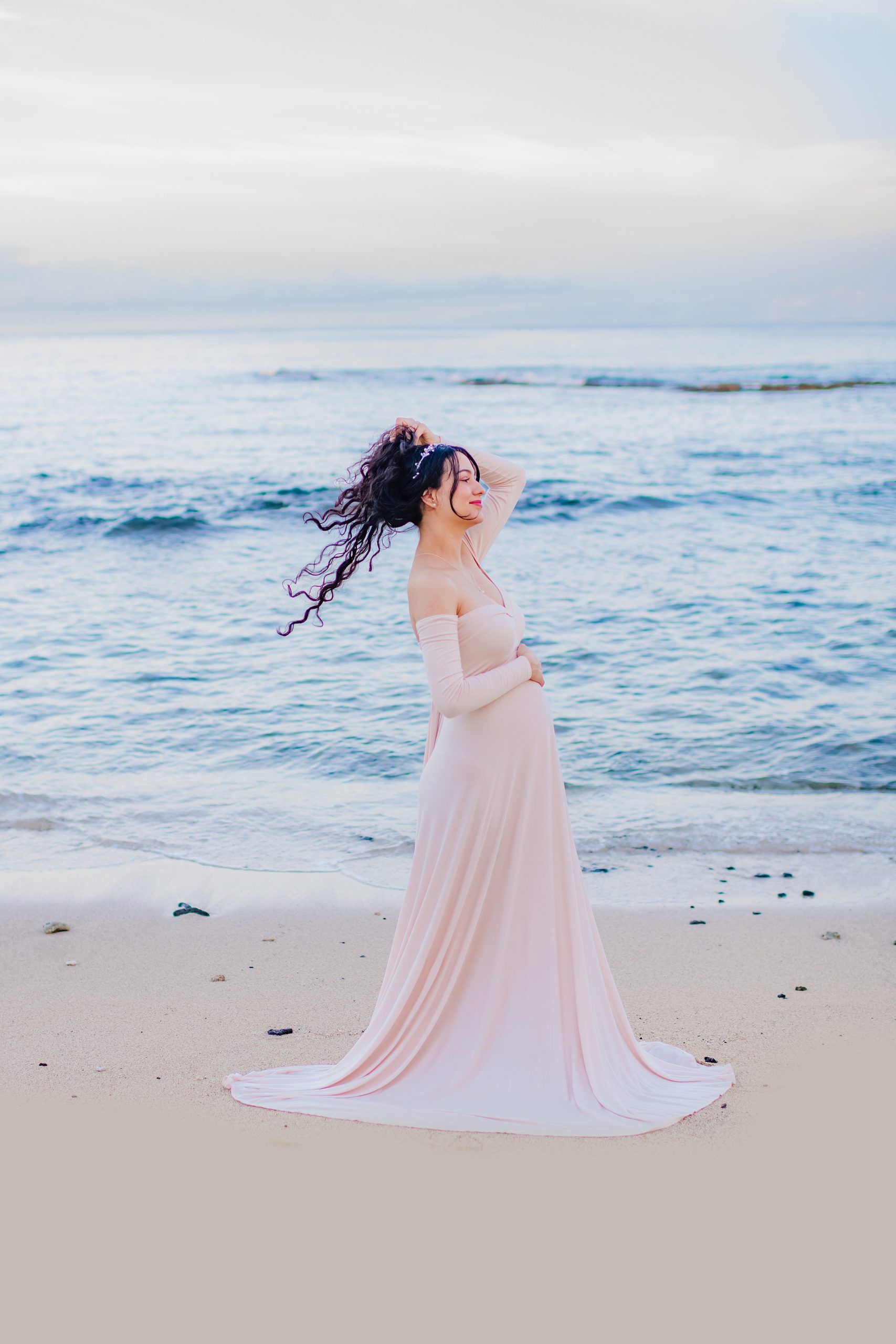 brunette with curly hair holds her pregnant belly during babymoon portraits in Hawaii with love + water photography