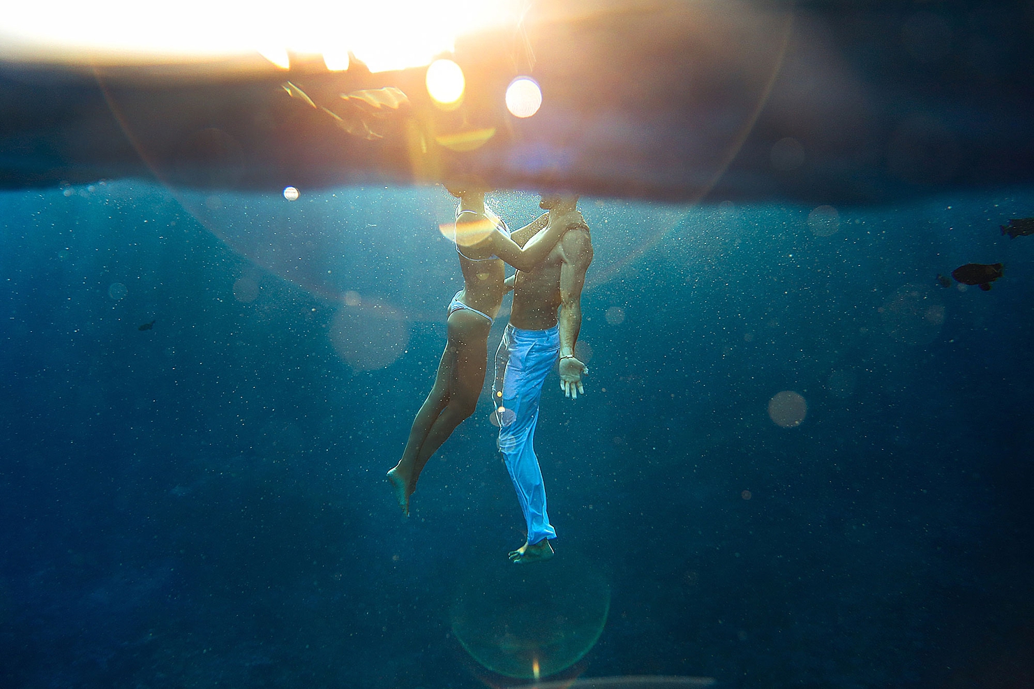 hawaii beach photoshoot ideas of underwater portrait of couple with arms outstretched and golden light filtering from above the surface