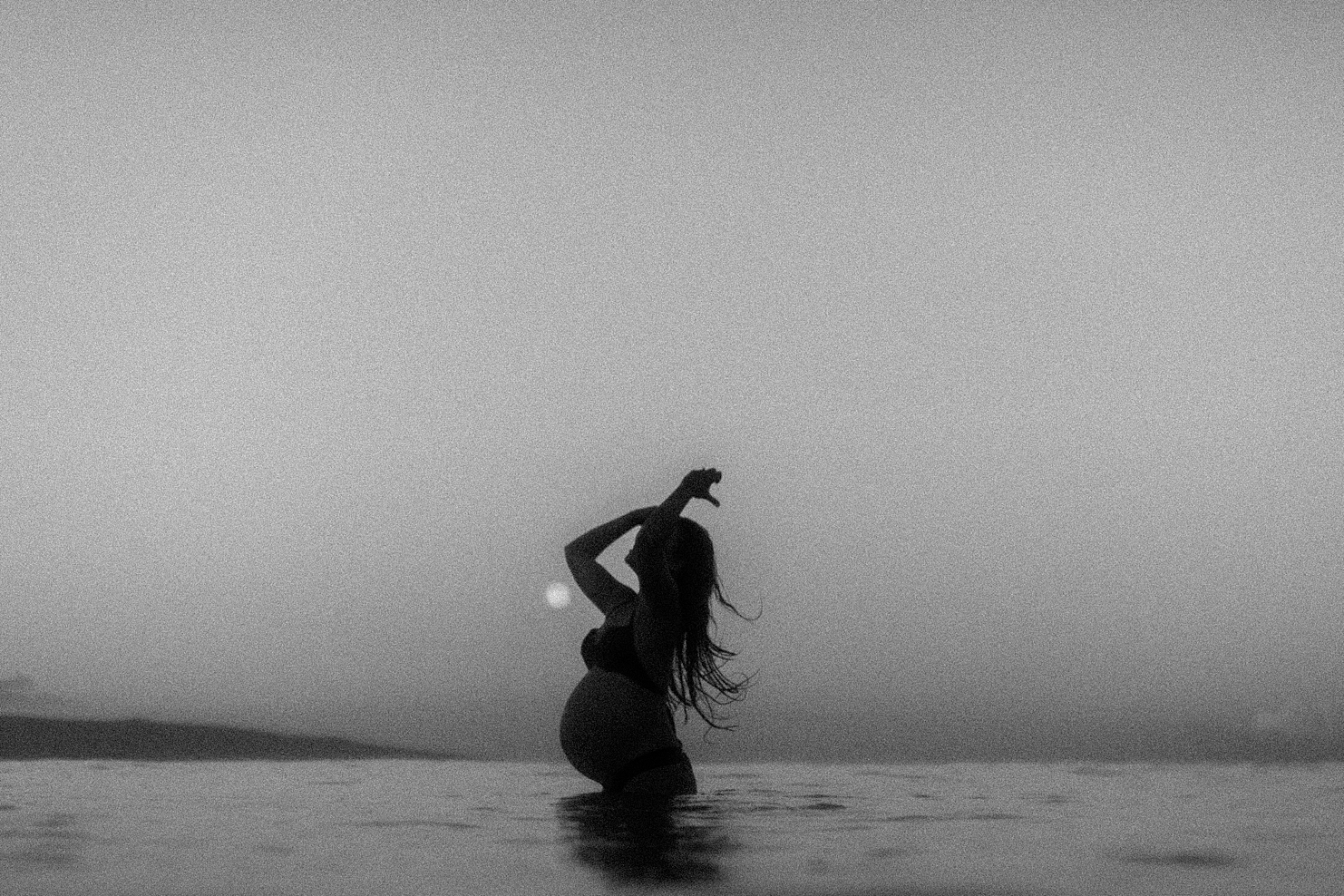 black and white grainy image of pregnant woman in the water during her maui maternity photoshoot