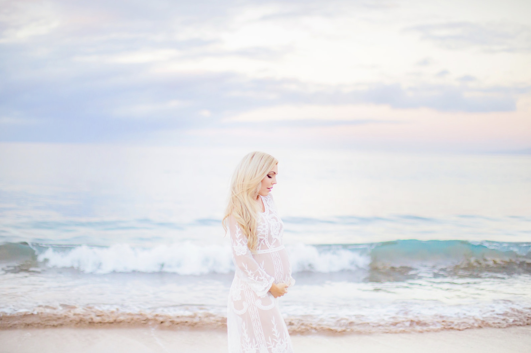 blonde woman looks down at her pregnant belly at sunrise in hawaii