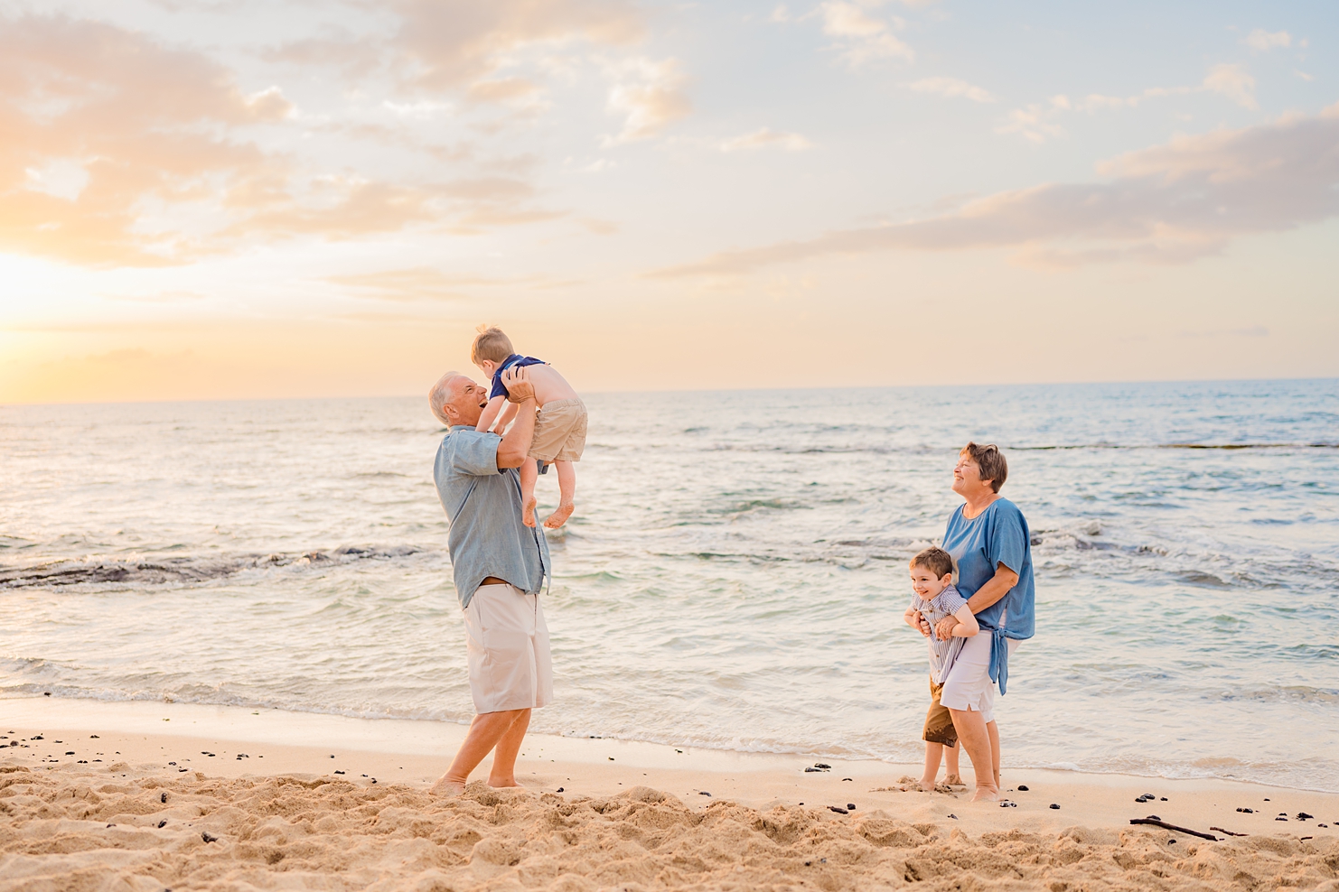 grandfather lifits his grandson into the air at sunset during a big island family photography shoot