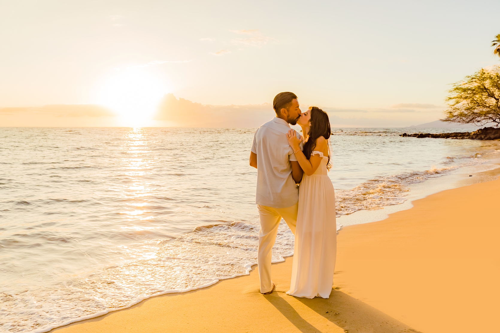 Woman in white dress kisses her husband during their beach photoshoot in Maui with love and water photography