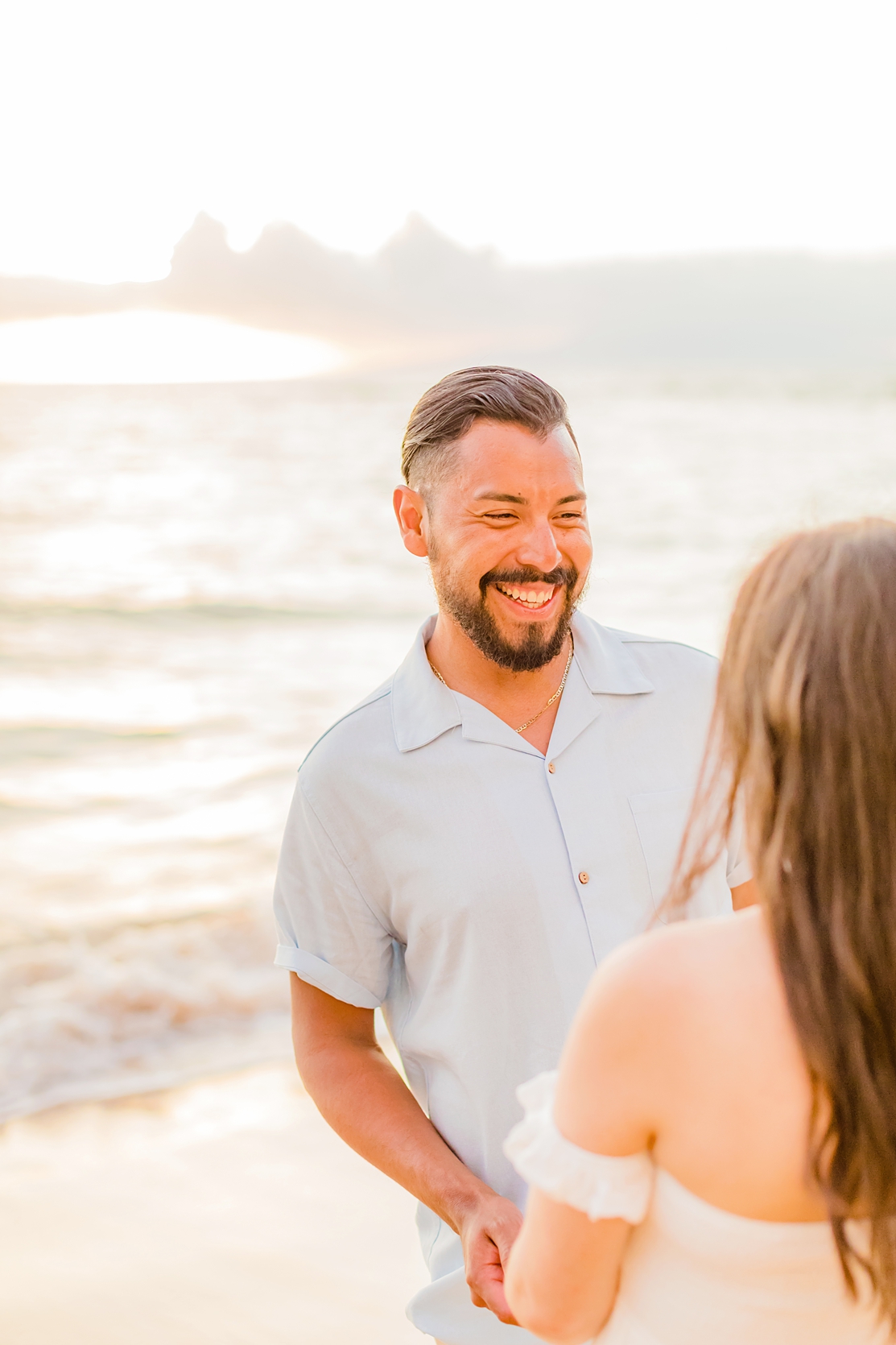 husband with dark brown hair and beard with short sleeve button up shirt smiles at his new bride while on honeymoon in hawaii
