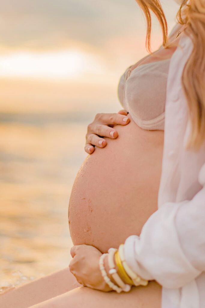 closeup maternity belly portrait of woman in white long sleeved button down shirt and bikini top