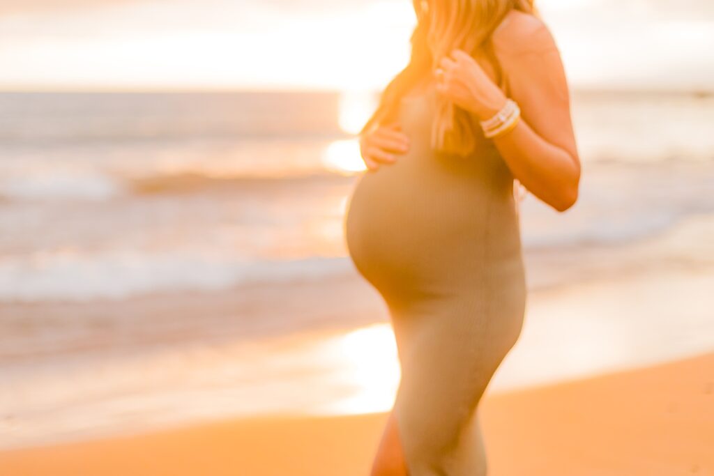 blurry image of pregnant belly backlit by the setting sun in hawaii