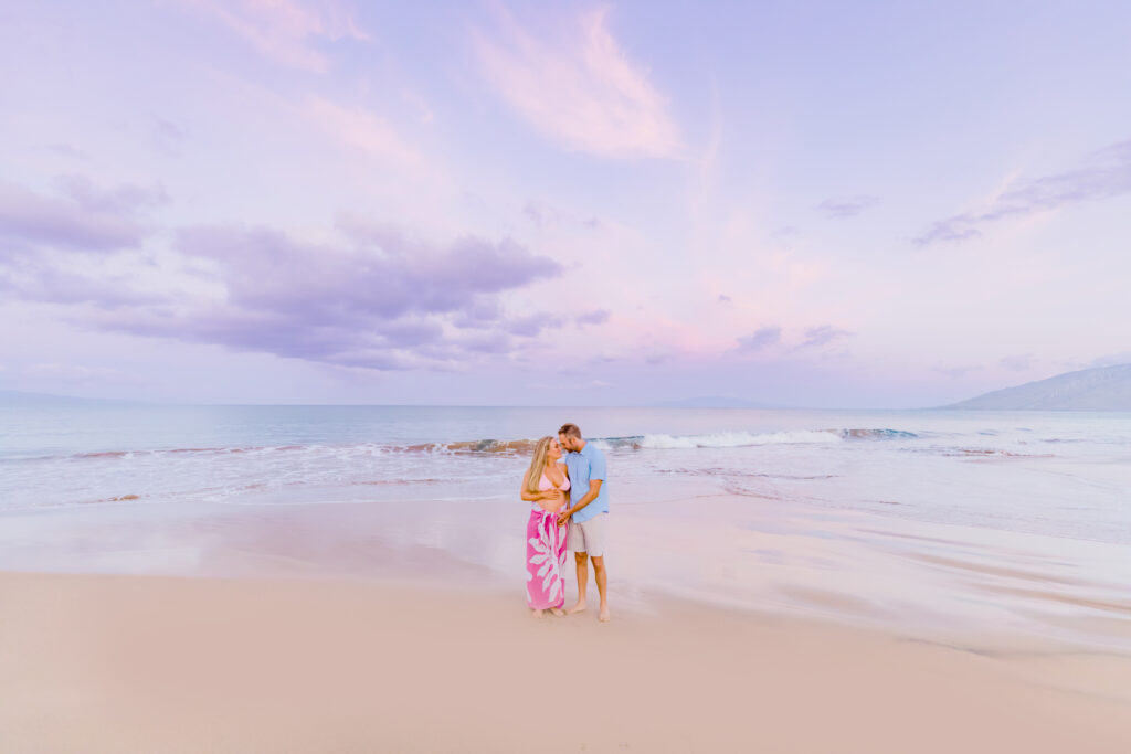 Couple poses at sunrise on the beach in Maui during their babymoon maternity shoot