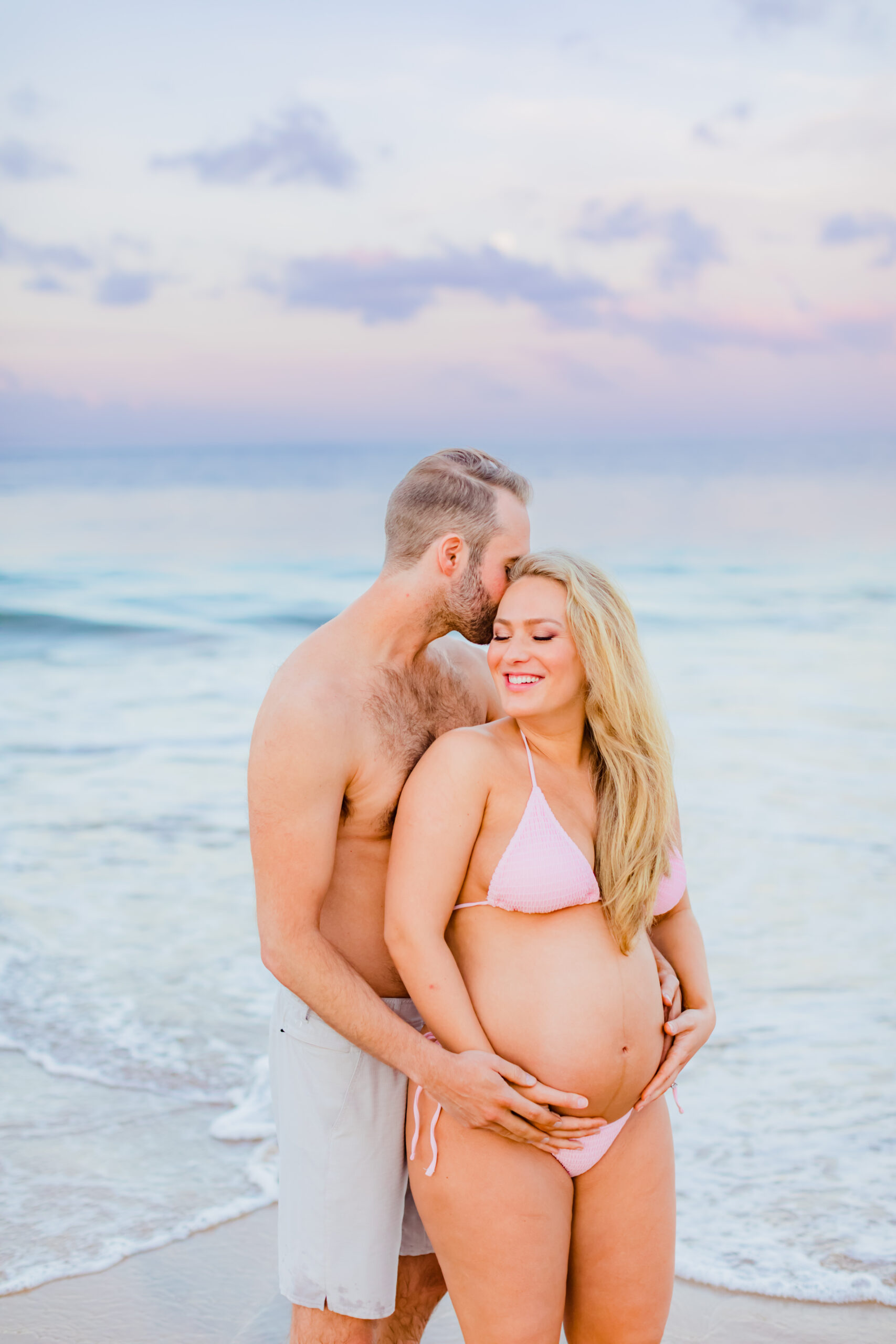 Partner holds his pregnant partner close during their beach maternity shoot in Maui