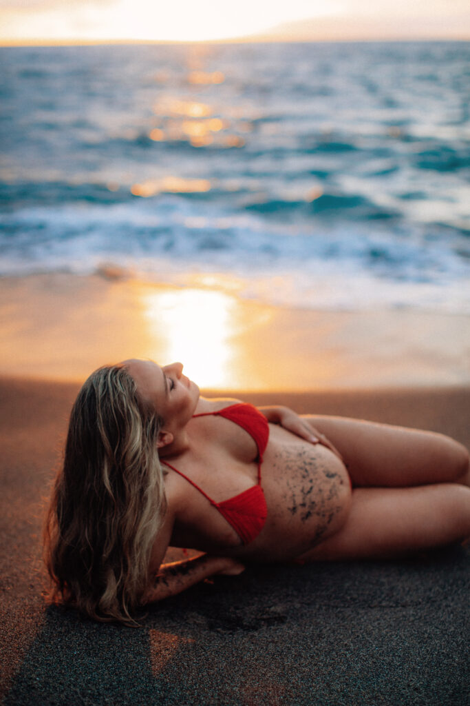 Sun setting over the Maui horizon as a woman poses while accentuating her pregnancy bump for photos