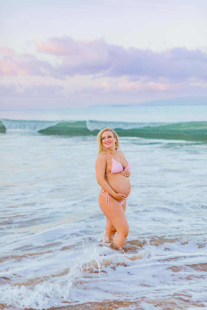 Pregnant woman in a pastel pink bikini smiles during her Maui pregnancy photo session