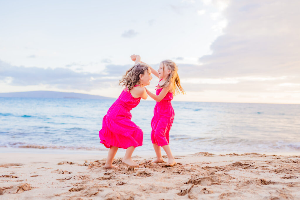 Sisters dance on the beach holding hands during their family session