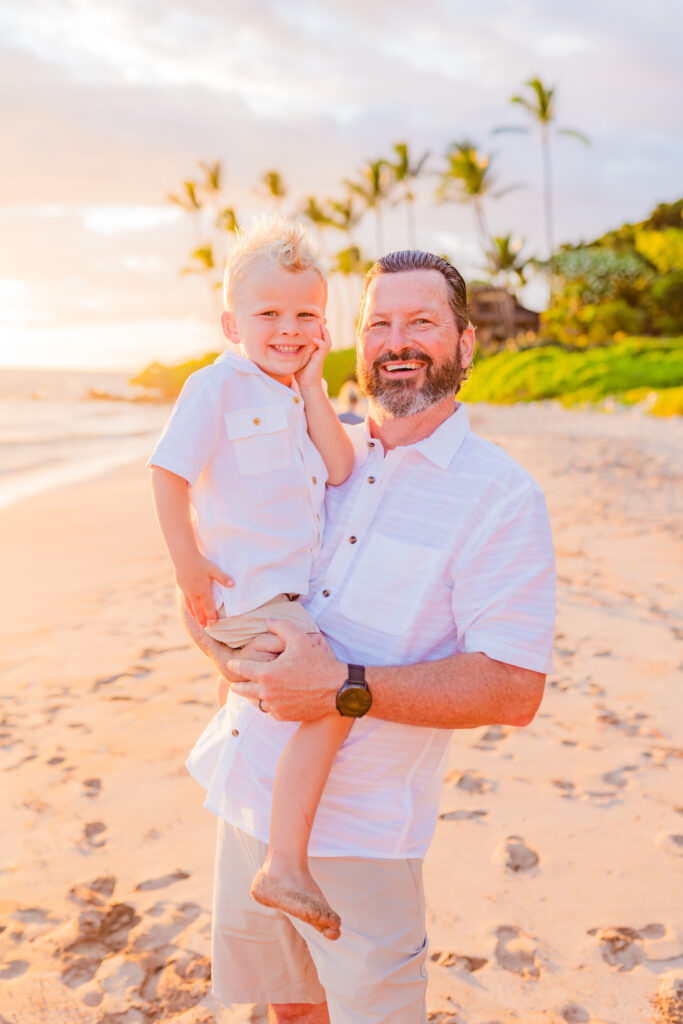 A dad holds his son up for a photo during their family photoshoot on the beach