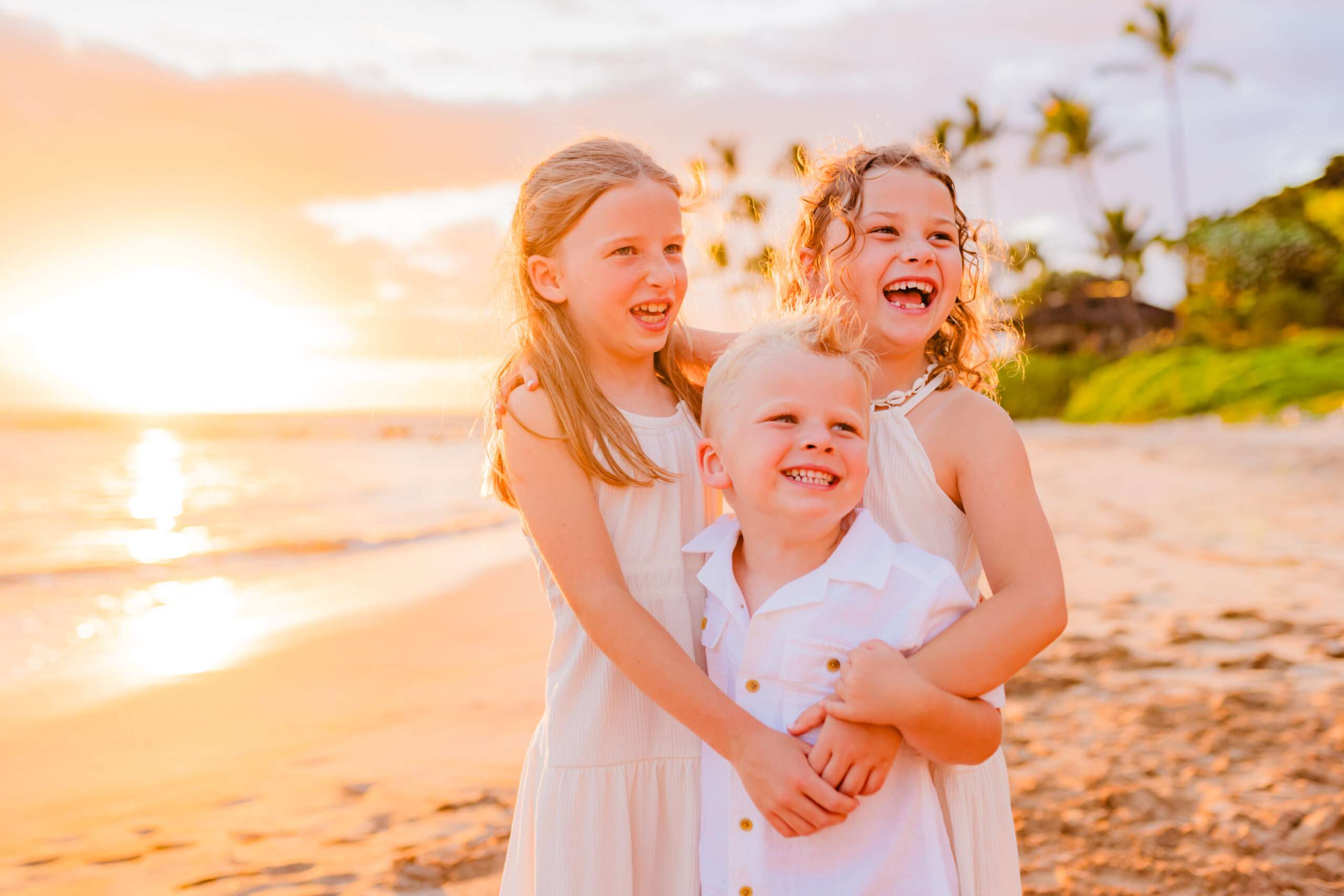 Three happy kids smile during golden hour at their beach family photoshoot